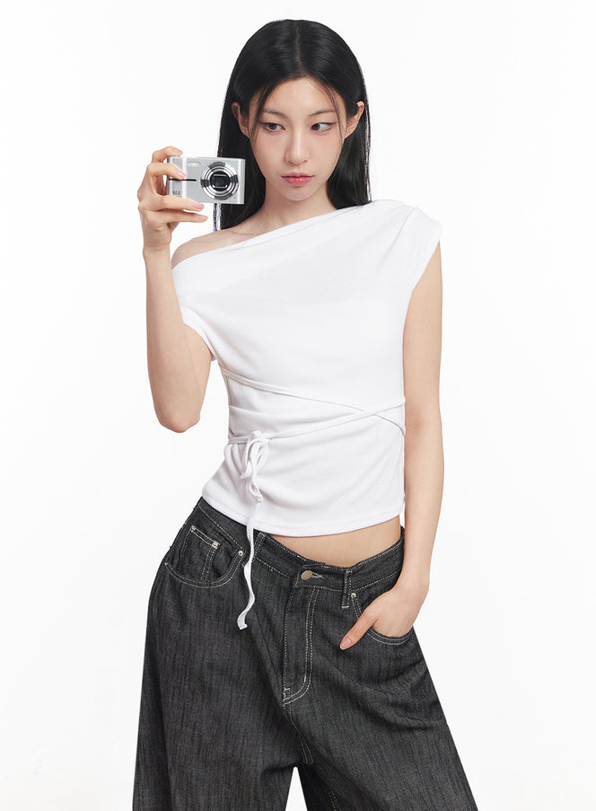 LEWKIN Asymmetric Short Sleeve Wrap Shirt IY516 in white, front close-up on model holding camera, one-shoulder crop top with crossover string tie at hem, paired with dark wide-leg jeans.