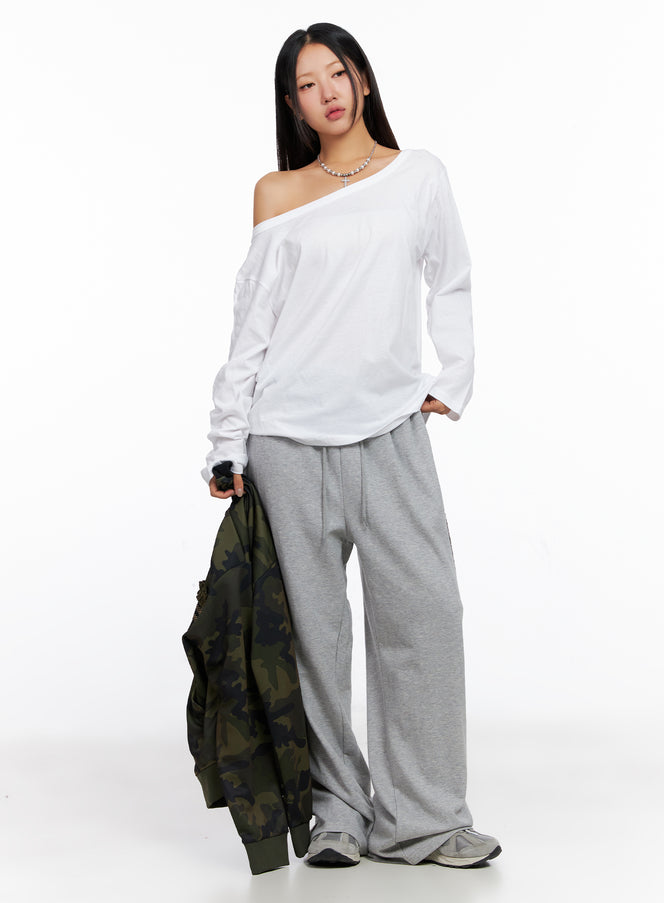 Relaxed Off-Shoulder Long Sleeve Top CO514 in white, full-length front shot on model, oversize casual cotton top, styled with grey wide-leg sweatpants and camo jacket held at side.