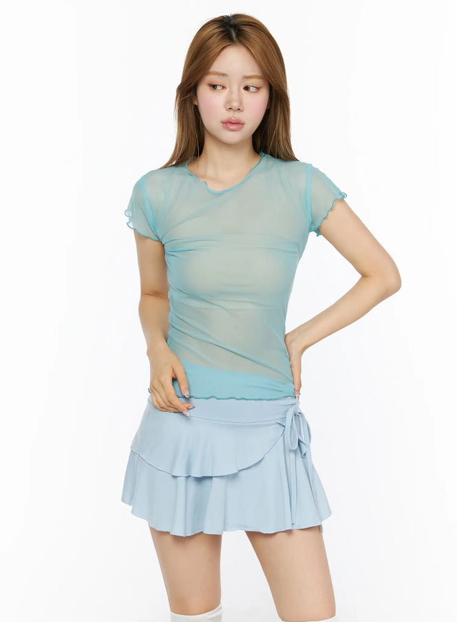 Sheer Short Sleeve Top CL501 mint front model shot, sheer ruched mesh tee with lettuce-edge neckline and sleeves, paired with light blue tiered ruffle mini skirt, hand on hip